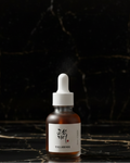 A small amber glass dropper bottle with a white label and white dropper cap, photographed on a marble black background.